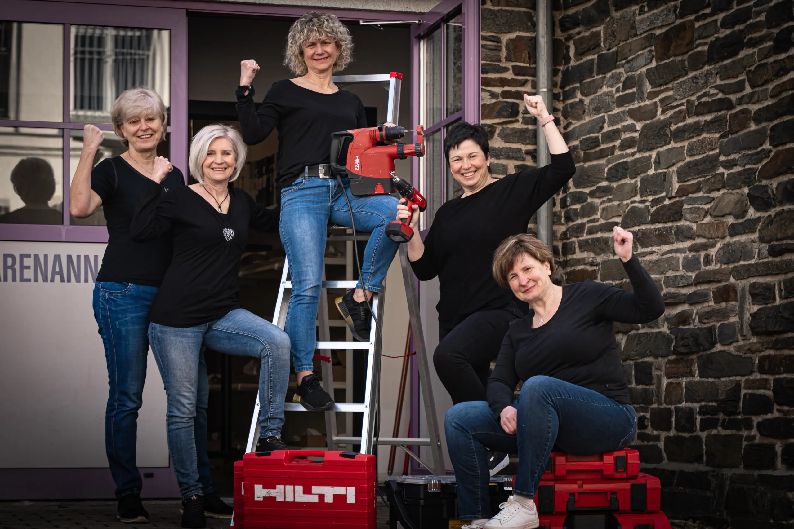 Unsere Montage-Mitarbeiterinnen mit Leiter und Werkzeug vor unserem Firmengebäude, mit motivierter, anpackender Pose